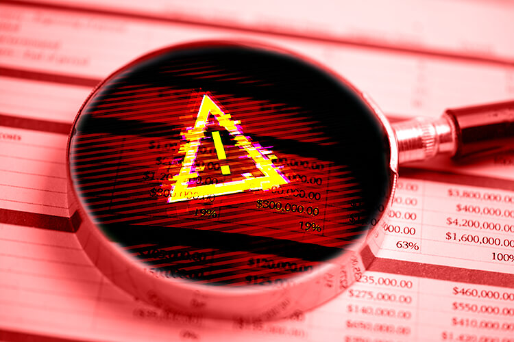 photo of magnifying glass with caution symbol, sitting on a printed financial report