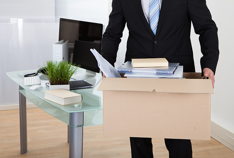photograph of man in an office carrying belongings in cardboard box